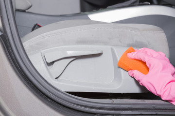 Chemical cleaning process. Hand in rubber protective glove with sponge cleaning a dirty car seat's plastic zone.