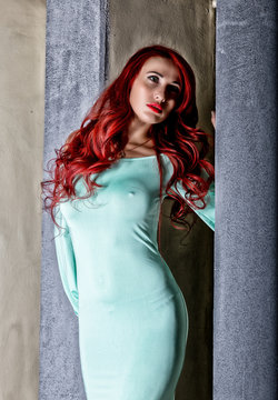 sexy beautiful redhead young woman with big boobs in a turquoise dress on a old gray wall background
