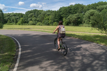 Naklejka premium Girl riding a bicycle. Back view. Forest and clouds in the background