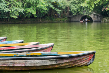 Old multicolored boats on a lake with trees and stone bridge in