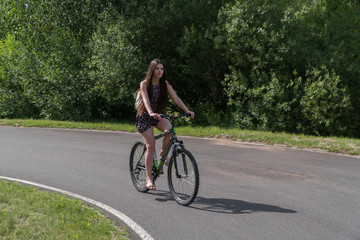 Girl riding a bicycle. Side view. Forest and clouds in the background