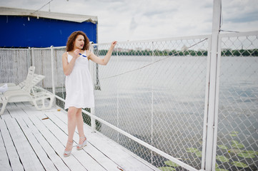 Portrait of a stunning girl posing on a white wooden harbour next to the water with her marine...