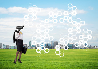 Camera headed woman standing on green grass against modern cityscape