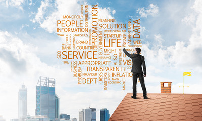 Young businessman standing on house roof and writing leadership skill concept. Mixed media