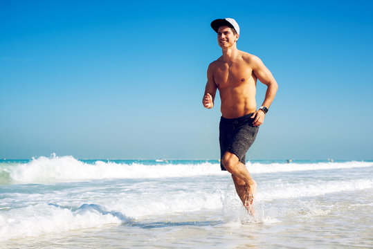 Muscular man athlete running on the beach.