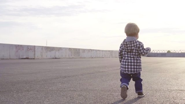 A little 2 year old baby boy is walking on sunset. Child make his first steps outdoor