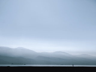 A man walks by the mountains and the sea at dawn