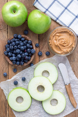 Green apple rounds with peanut butter and and blueberries on wooden table, vertical, top view