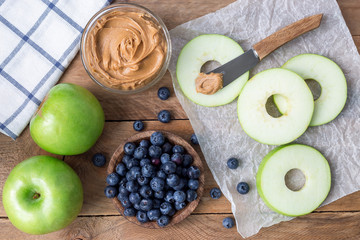 Green apple rounds with peanut butter and and blueberries on wooden table, horizontal, top view