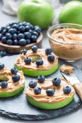 Green apple rounds with peanut butter and and blueberries on slate board, vertical