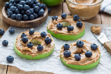 Green apple rounds with peanut butter and and blueberries on wooden table, horizontal