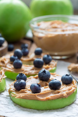 Green apple rounds with peanut butter and and blueberries on wooden table, vertical