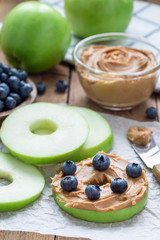 Green apple rounds with peanut butter and and blueberries on wooden table, vertical