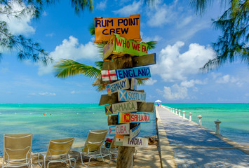 Colorful signpost by the Caribbean sea and a jetty at Rum Point, Grand Cayman, Cayman Islands - obrazy, fototapety, plakaty