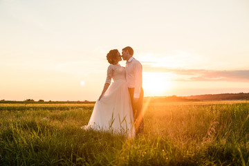 Young kissing wedding couple enjoying romantic moments outside on a summer meadow