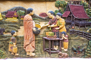 Thai lifestyle stone carving on the wall (Offerings in a monk's alms bowl) at at Wat Tai Phra Chao Yai Ong Tue,Ubonratchathani Province,Thailand.