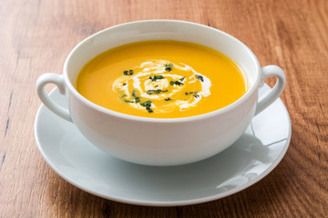 Pumpkin soup in white bowl on wooden table
