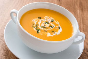 Pumpkin soup in white bowl on wooden table
