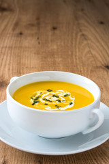 Pumpkin soup in white bowl on wooden table
