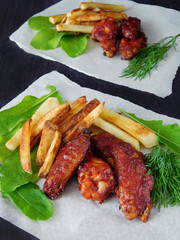 French fries and grilled chicken wings on the green salad on a piece of paper