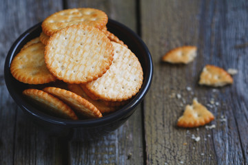 Black ceramic bowl with salted crackers on an old wooden table.