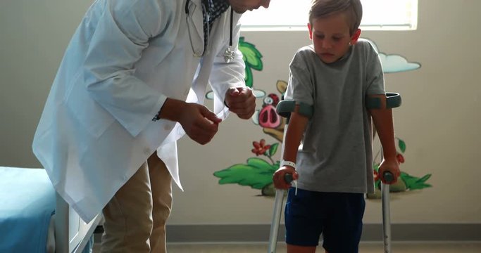 Male doctor assisting injured boy to walk with crutches