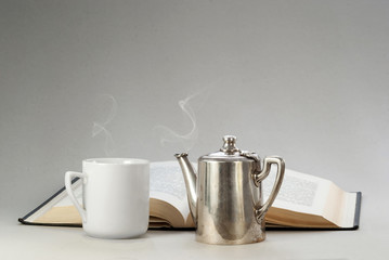 Vintage white cup and a silver teapot with hot drinks on the background of the books. Reading, background for postcards, poster, website. Clean composition.