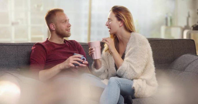 Young boyfriend removing a wisp from his girlfriend while drinking tea on a couch