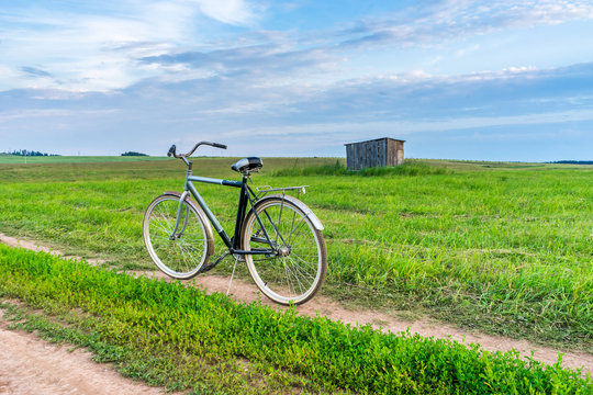 Old bicycle on the road in a field of mown grass at sunset