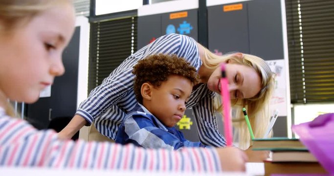 Teacher helping schoolboy with her homework in classroom