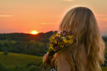 Naklejka premium Background landscape girl holding a bouquet with wildflowers of herbs in her hand and watching the sunset sunrise on the horizon