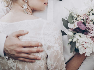 stylish wedding bride with bouquet. modern bride hugging groom, lips and earrings close up. fine...