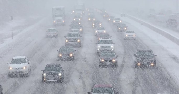 Cars driving in traffic on a snow covered road during a winter blizzard