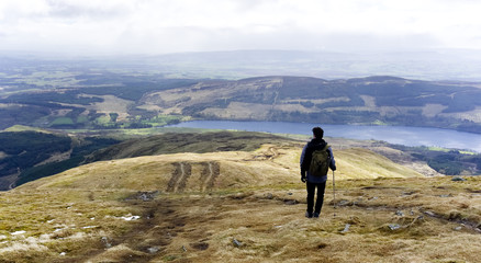 Hill walker on a country path looking down towards a lake in a country landscape at Pentland Hills, Edinburgh, Scotland 