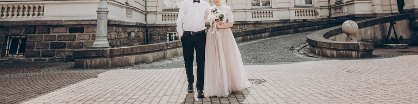 stylish wedding couple with bouquet. modern bride and groom holding fashionable bouquet at old stairs at castle. fine art wedding photo, romantic moment, long edge