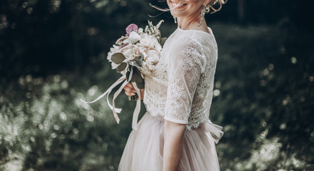 stylish wedding bride with bouquet and amazing modern dress. bride posing and smiling in sunny garden, lips and earrings close up. fine art wedding photo, romantic moment, long edge