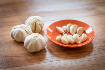 White garlic bulb in an orange plate and leaves of green parsley