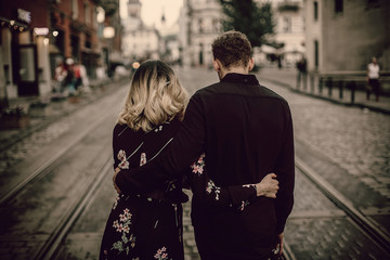Fototapeta premium stylish gypsy couple in love walking and hugging in evening city street. woman and man gently embracing, romantic french atmospheric moment. love mood. back view