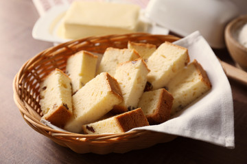 Wicker basket with delicious sliced butter cake on wooden table
