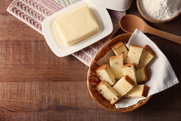 Wicker basket with delicious sliced butter cake on wooden table