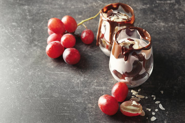 Delicious yogurt parfait with chocolate sauce in glasses and grapes on table
