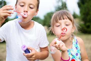 Close-up portrait of two eastern european small children blowing bubbles outdoors in park on summer day