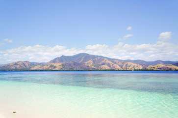 Empty white sand beach at midday overlooking broad island with green vegetation in te ocean, Flores Indonesia.