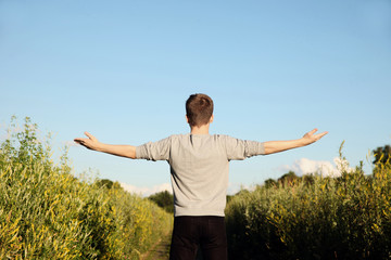 Young man stands with his hands up and looks at the sky