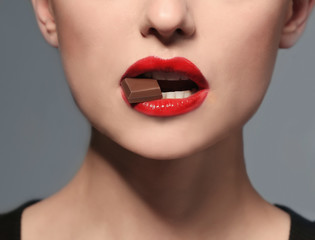 Beautiful young woman with bright lips eating piece of chocolate, closeup