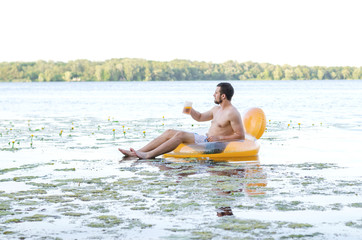 A man drinks beer sitting in a rubber ring in the water, free space.