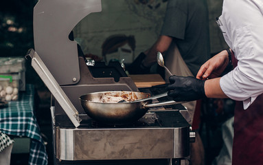 grilling barbecue steak. man holding steel spoon and roasting meat on big pan. chef in form and gloves cooking smoked juicy beef pork. street food festival. summer picnic