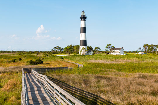 Fototapeta Wooden ramp over marshland, with a boardwalk trail to the Bodie Island lighthouse and surrounding buildings, on the Outer Banks of North Carolina near Nags Head.  