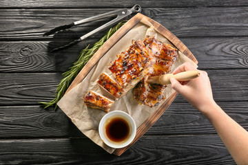 Woman adding soy sauce to roasted pork ribs on wooden board