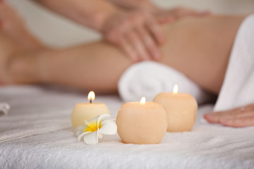 Burning candles with beautiful flower and blurred woman having legs massage in spa salon on background